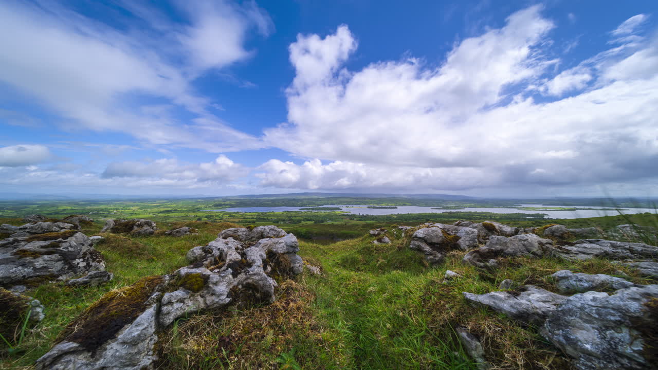 Timelapse di un paesaggio rurale con formazione rocciosa in primo piano, colline e lago in lontananza durante una giornata nuvolosa e soleggiata, visto da Carrowkeel, nella contea di Sligo, in Irlanda