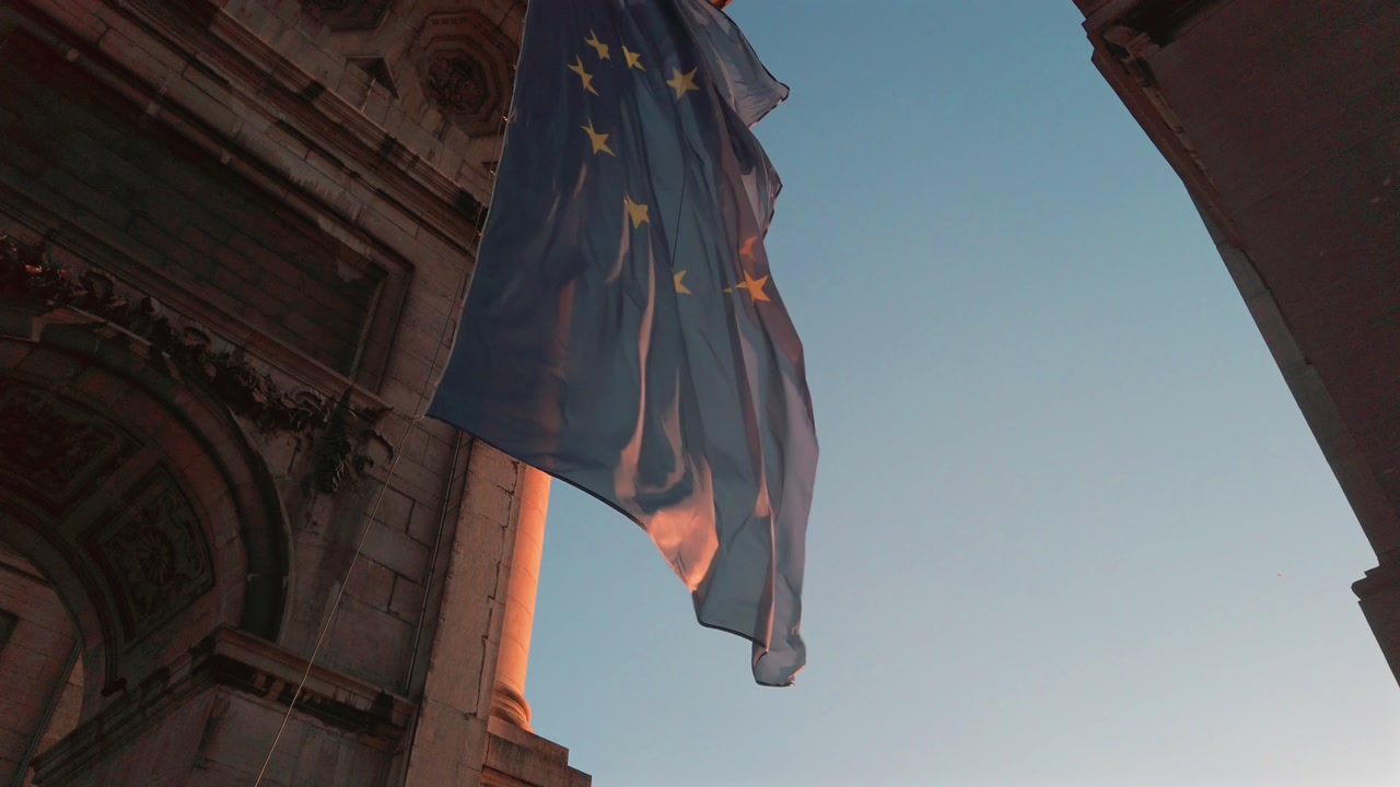 Slow motion capture of EU flag fluttering under the Cinquantenaire Arch in Brussels during sunset
