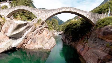 Fpv-luftdrohnenaufnahmen-Entlang-Des-Flusses-Mit-Klarem-Wasser-Und-Unter-Der-Brücke-Nach-Lavertezzo,-Schweiz