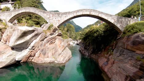 fpv aerial drone footage along river with clear water and under bridge to lavertezzo, switzerland