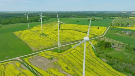Aerial-establishing-view-of-wind-turbines-generating-renewable-energy-in-the-wind-farm,-blooming-yellow-rapeseed-fields,-countryside-landscape,-sunny-spring-day,-wide-drone-shot-moving-backward