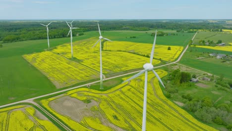 Luftaufnahme-Von-Windturbinen,-Die-Im-Windpark-Erneuerbare-Energie-Erzeugen,-Blühende-Gelbe-Rapsfelder,-Ländliche-Landschaft,-Sonniger-Frühlingstag,-Breite-Drohnenaufnahme,-Die-Sich-Rückwärts-Bewegt