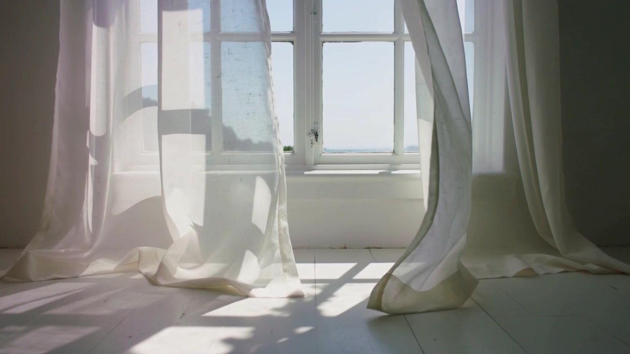 Billowing sheer curtains lifting inward from breeze in sunlit room, revealing blue sky and latch