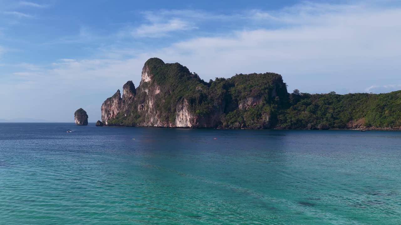 Ampia ripresa aerea di scogliere calcaree tropicali e acqua cristallina turchese sotto un cielo azzurro.