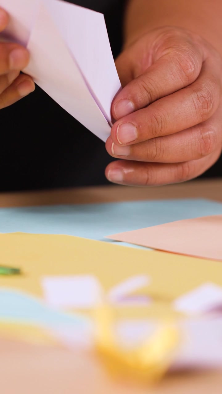 Close-up shot of hands carefully folding white paper into an origami plane on a table