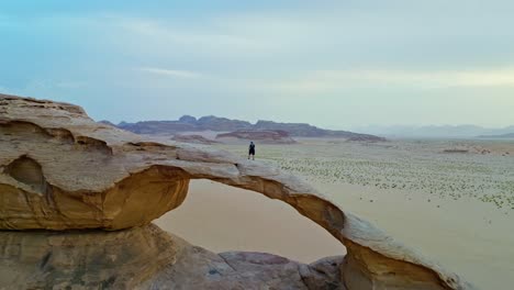 Cinematic-View-Of-Man-Standing-On-Rock-Formation-In-Wadi-Rum-Desert-In-Southern-Jordan---drone-shot