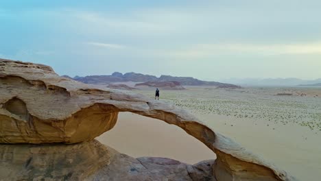 vista cinematográfica de un hombre de pie en una formación rocosa en el desierto de wadi rum en el sur de jordania - toma de avión no tripulado