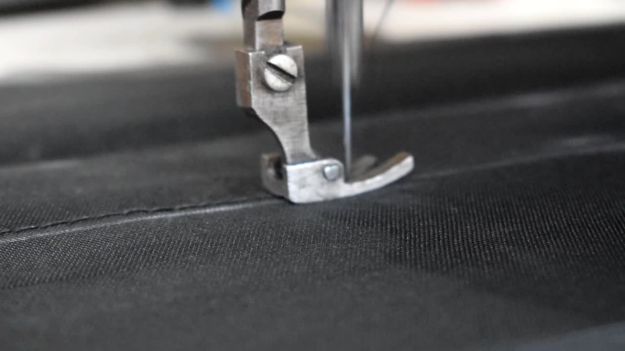 바늘과 실을 꿰매는 검은 데님 직물로 재봉틀의 노루발을 닫습니다 - 매크로