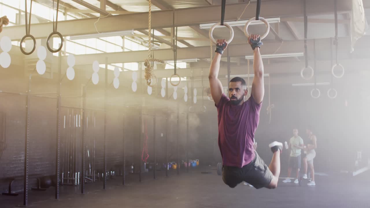 hombre biracial enfocado haciendo flexiones en los anillos del gimnasio en el gimnasio, en cámara lenta