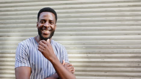 young african american man smiles broadly, standing before a metal shutter with copy space