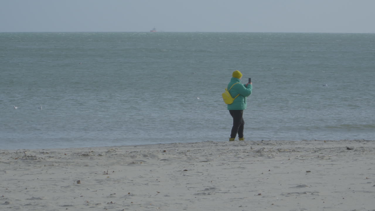 잔잔한 해변이 있는 모래사장을 지나가는 스마트폰을 가진 여자