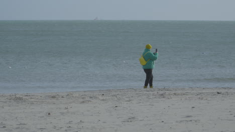 a woman with smartphone passing by sandy shore with calm beach