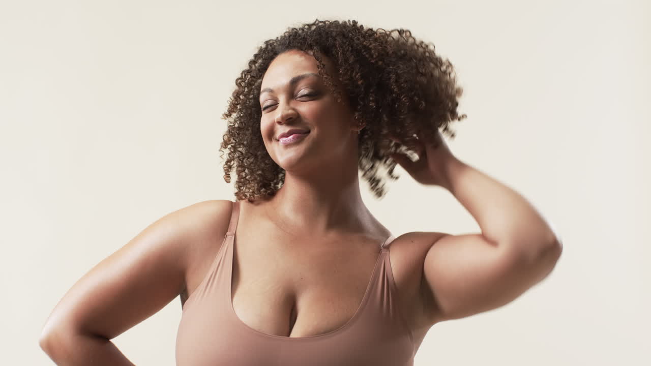 Young biracial plus size woman with curly hair posing confidently in studio