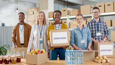 grupo multiétnico de voluntarios empacando cajas con comida y ropa en un almacén de caridad y sonriendo a la cámara