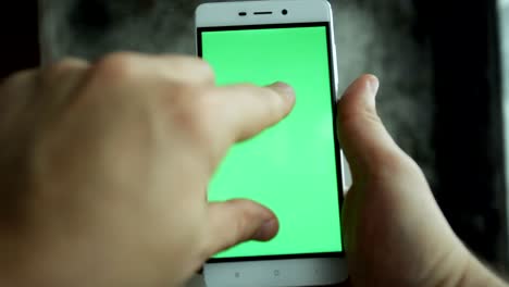 hombre de primer plano con la mano sosteniendo y tocando el teléfono con pantalla verde vertical