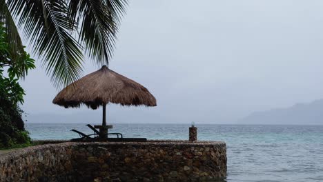 lonely thatched roof sun parasol with nobody around on a remote tropical island during monsoon season with grey, wet and raining weather conditions