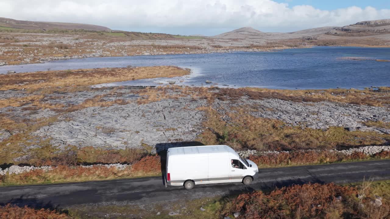 Delivery Van Traveling On The Road Along The Lake In The Burren in Irish Boirinn, County Clare, Ireland. - aerial shot