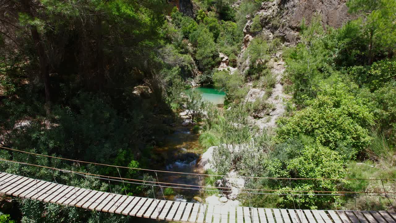 Passerella sospesa in legno su un ruscello di montagna con acque turchesi e colorate