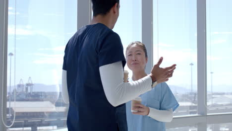 Young-Asian-healthcare-worker-and-biracial-healthcare-worker-converse-in-a-bright-hospital