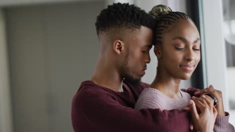 African-american-couple-standing-at-window-and-hugging
