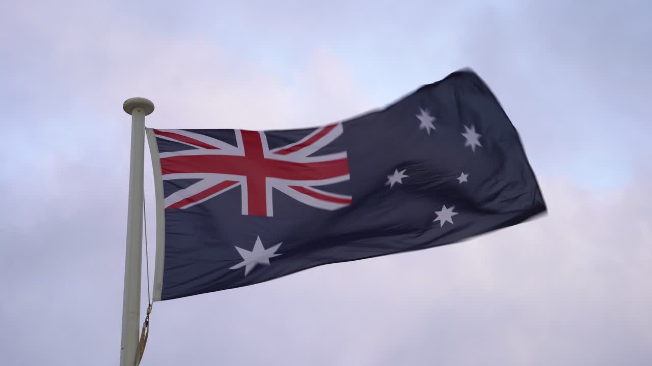 bandera de australia ondeando contra el cielo, bandera azul australiana, campo azul con union jack en el cuarto superior del polipasto, una gran estrella blanca de siete puntas de la comunidad y constelación de la cruz del sur