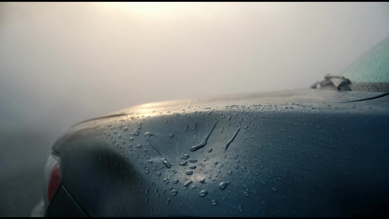 Primo piano di un cofano auto coperto di gocce di pioggia nella nebbia fitta