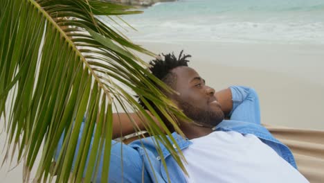 side view of african american man relaxing in a hammock on the beach 4k