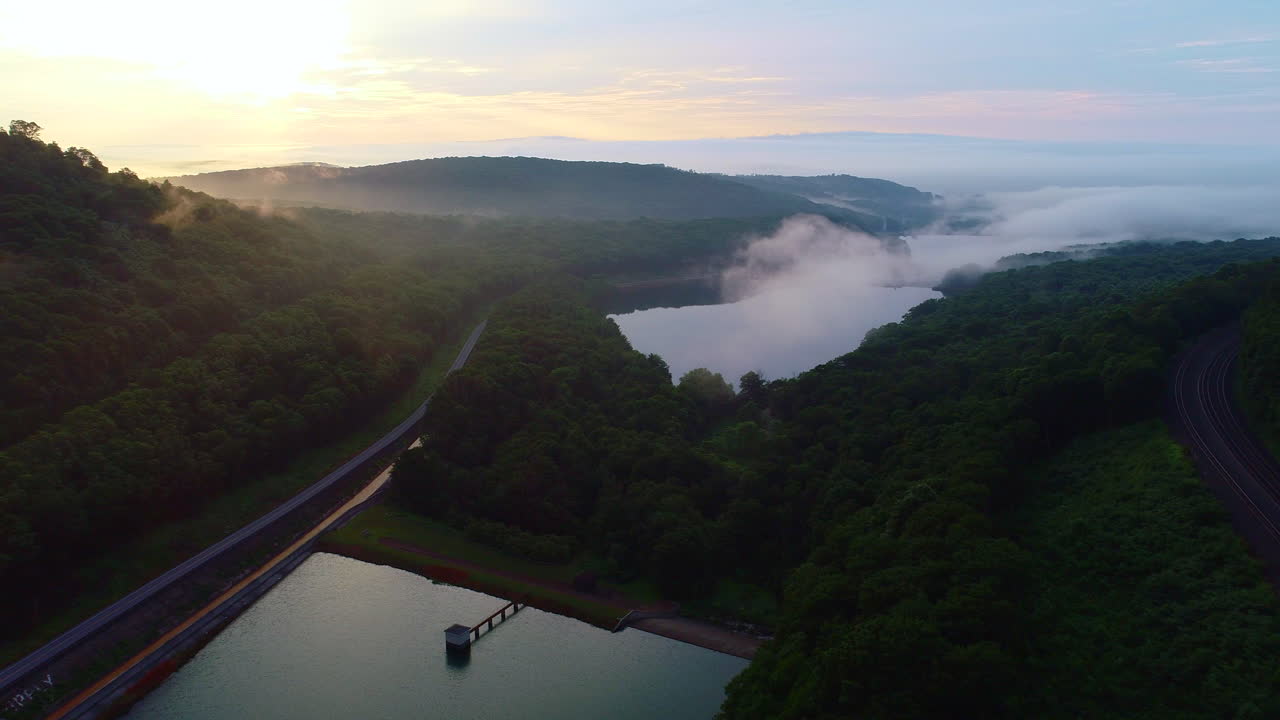Drone flying forward over a lake and fores during the early morning.  A layer of mist-clouds is hovering over the lake