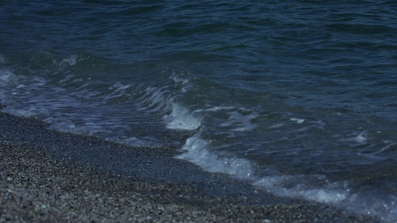 Small waves roll in on a pebble beach in Marbella Spain, 4K slow motion