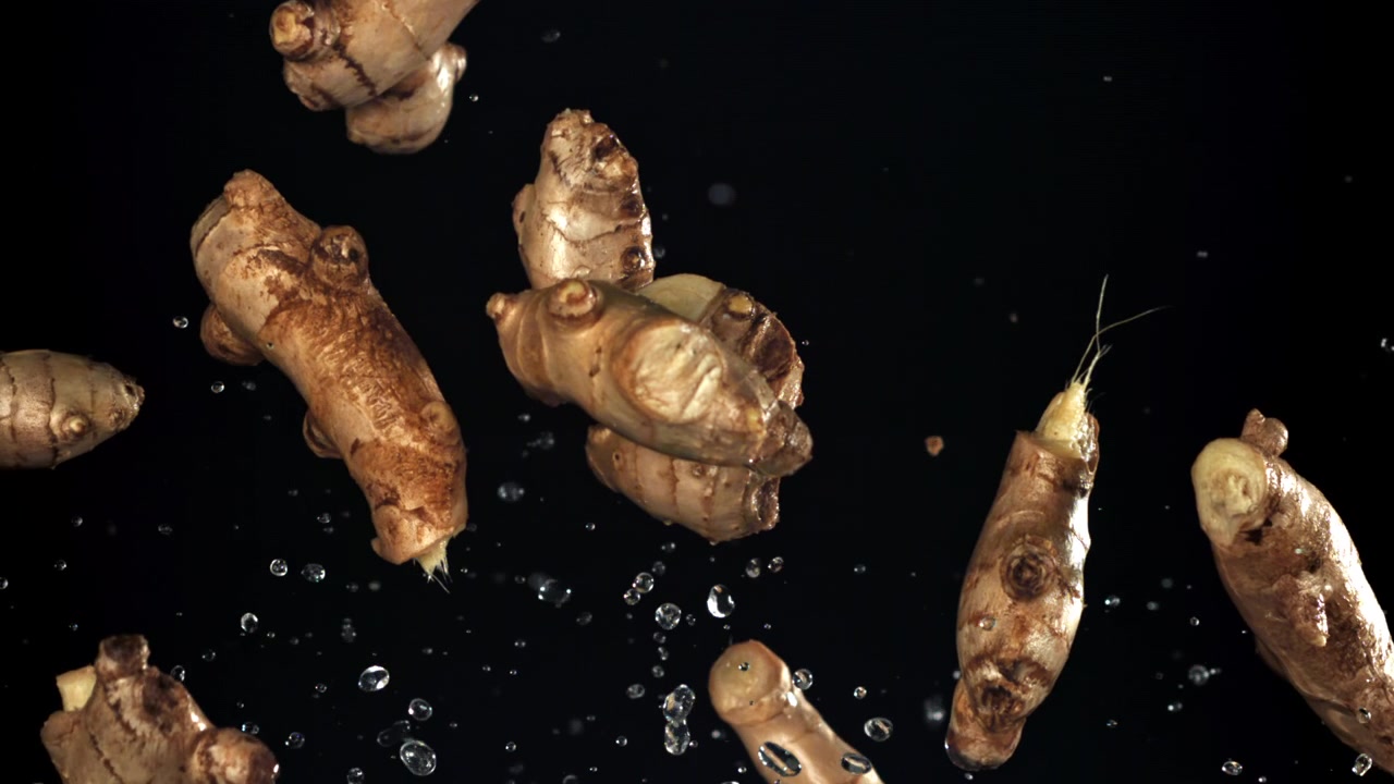Fresh Ginger Roots Falling with Water Drops in Slow Motion