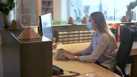 receptionist - office employee works with face mask on a computer in the reception area - coronavirus tourism footage