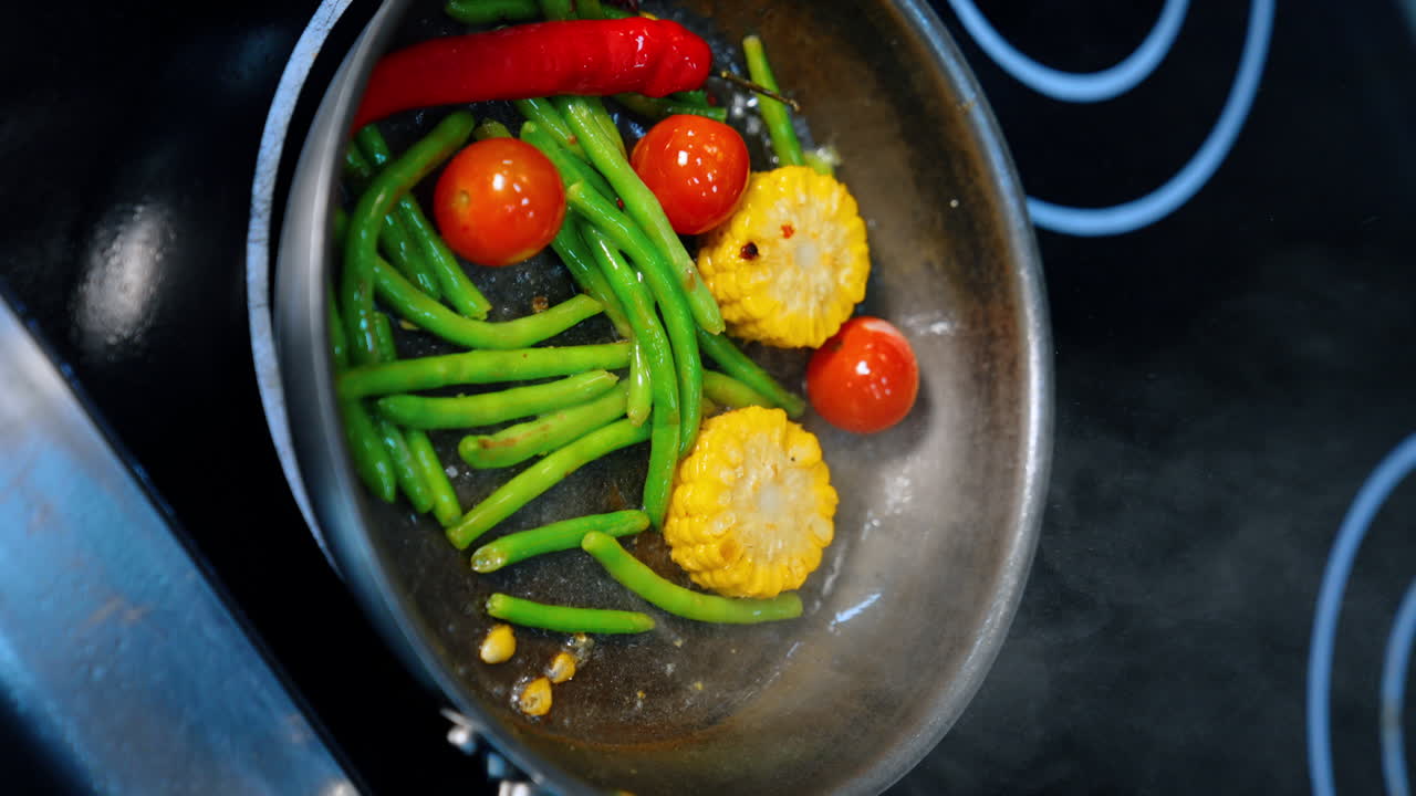 Cooking vegetables on the frying-pan. Maize, beans, chili pepper and tomatoes are fried together. Vertical screen. Close up.