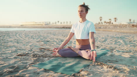 una joven tatuada meditando en la playa.