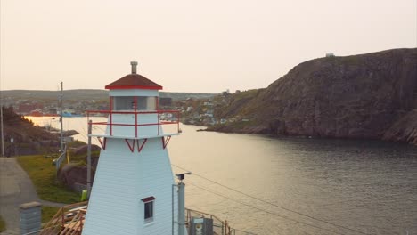 Aerial-view-of-lighthouse-on-coast-with-golden-light-reflected-on-calm-water-below