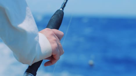 Closeup-on-man-resting-hand-on-trolling-fishing-rod,-rack-focus-to-Caribbean-Sea