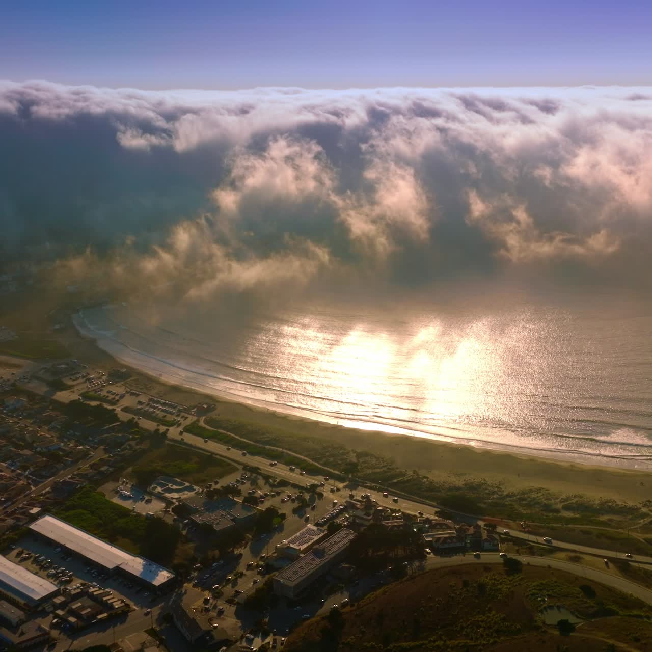 Huge wave of thick white fog moving from the ocean to the beach. Little residential area at the coastline of Montara, California, USA from aerial perspective