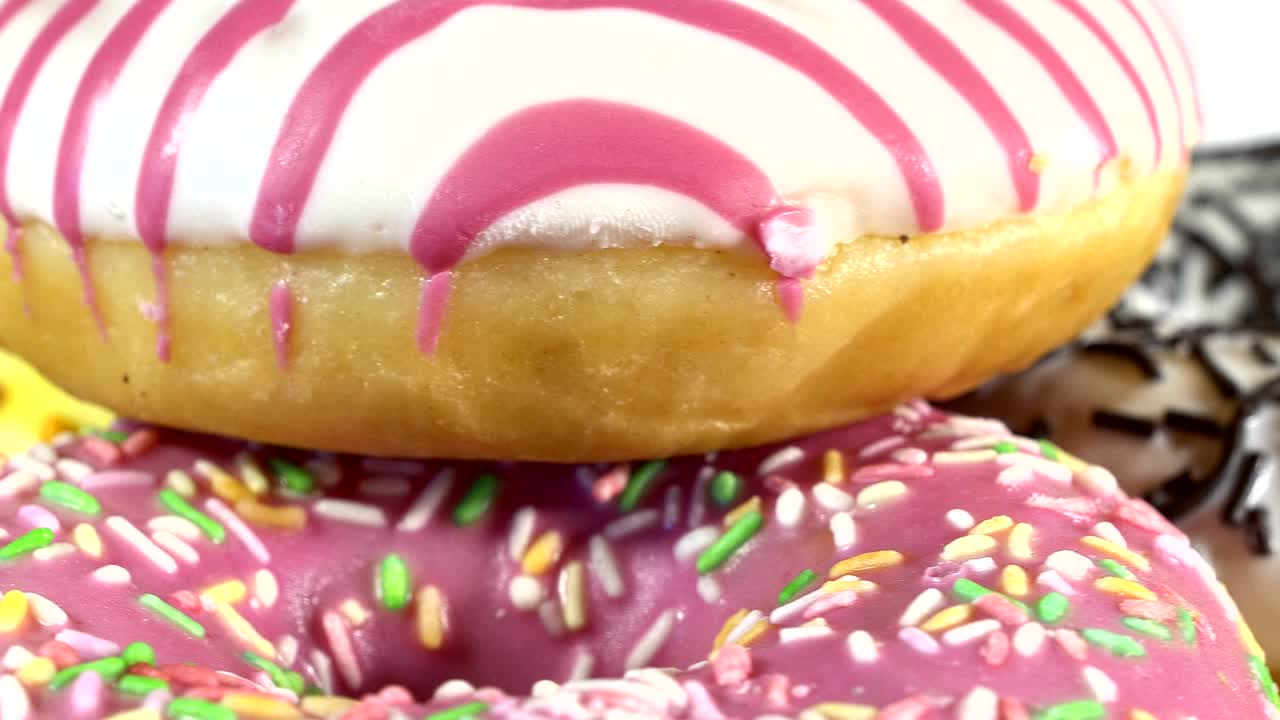 rosquillas giratorias con diferentes rellenos en la mesa. deliciosa rosquilla dulce girando en un plato. rosquilla brillante y colorida macro disparo de primer plano girando sobre un fondo blanco. bucle sin costuras.