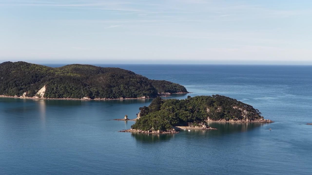 Luftaufnahme – zwei üppig bewaldete Inseln, die aus einem ruhigen blauen Meer unter klarem Himmel auf der Südinsel Neuseelands aufsteigen.