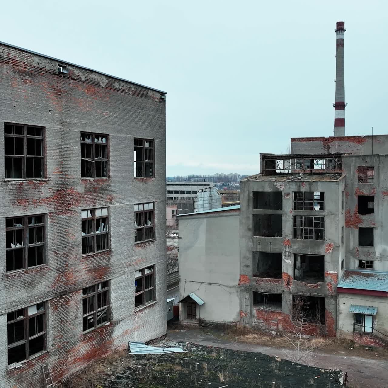 Damaged ruins of past big plant. Forlorn wrecked emptied buildings with no windows and old brick walls. Blue clear sky at the background