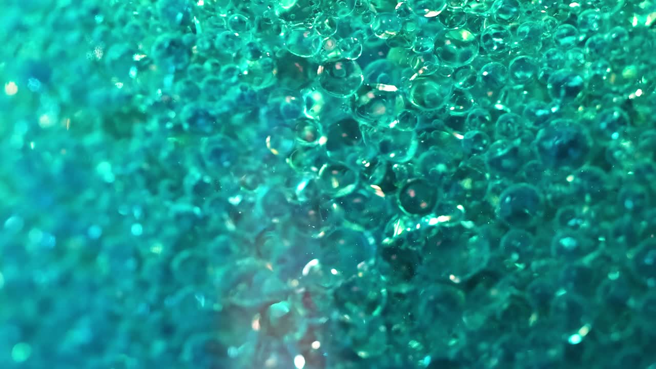 A detailed view of tiny, shimmering bubbles moving in a vibrant aqua liquid.