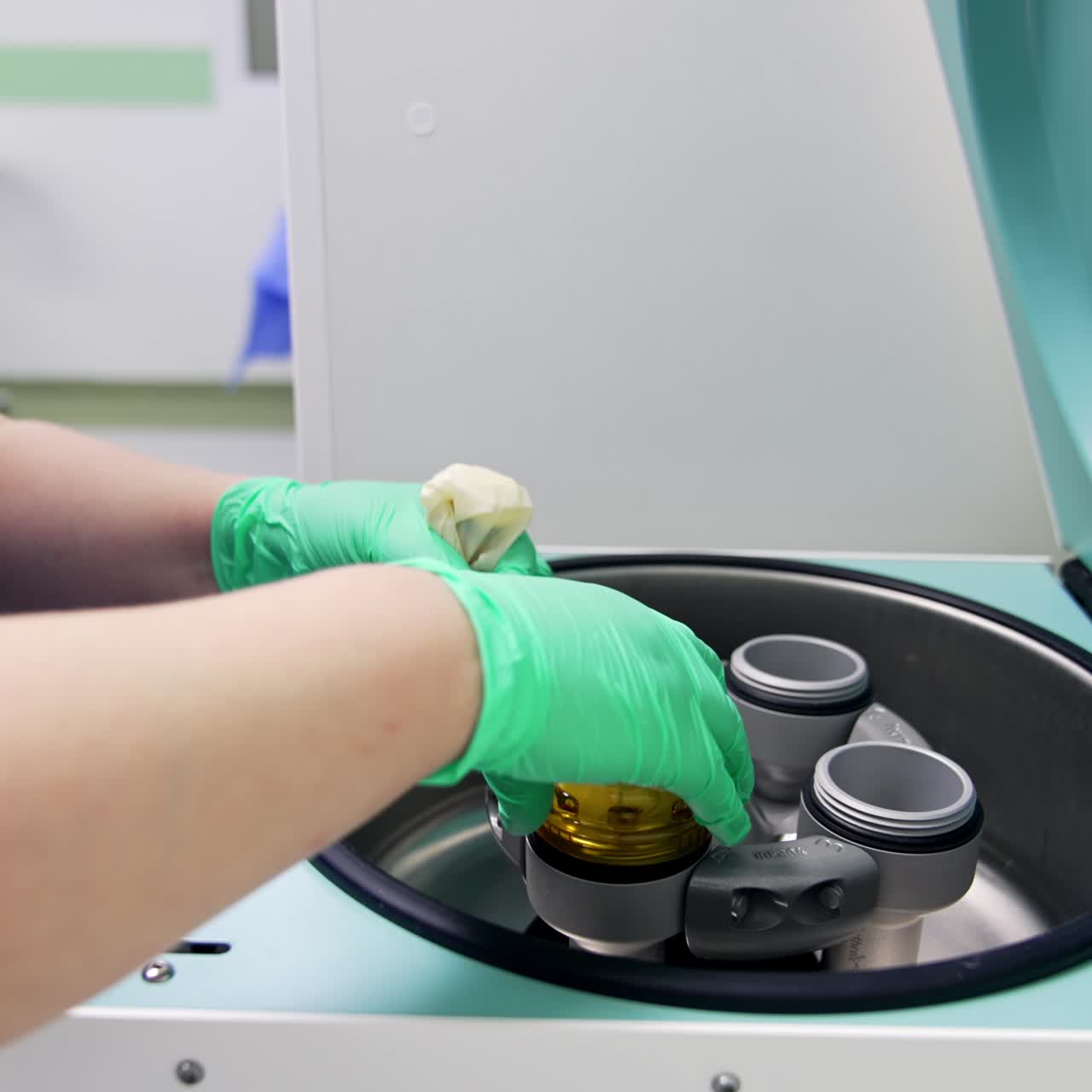 Apparatus centrifuge in modern laboratory of a hospital. Female nurse's hands put test tube in latex gloves into reservoirs of machine