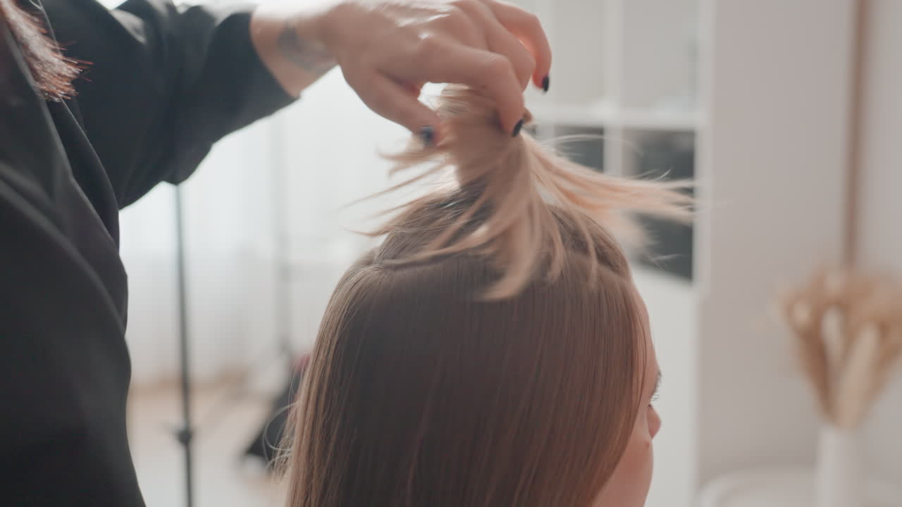 Primo piano di acconciatura in un salone luminoso, stilista divide ciocche bionde con mani delicate, fissa le sezioni con una clip per formare un elegante chignon, luce naturale soffusa, interni moderni e tranquilli, dettagli passo dopo passo