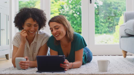 pareja de mujeres del mismo sexo o amigos en casa relajándose en el salón con una tableta digital y bebiendo café