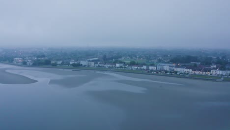 Costa-Urbana-Mística:-Vuelo-Aéreo-Alrededor-De-La-Playa-De-Sandmount-Con-Niebla-Durante-La-Marea-Baja-En-Un-Día-Oscuro-Con-Paisaje-Urbano-Y-Caminantes-De-Playa