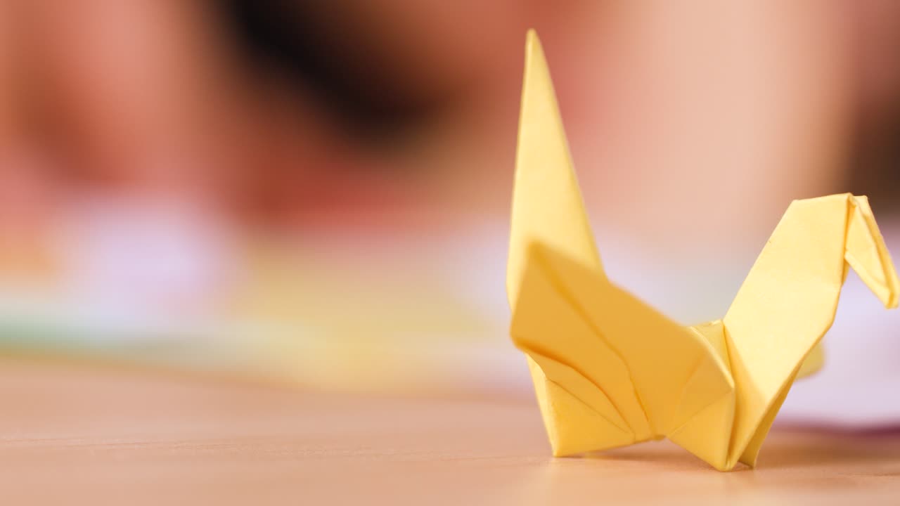 Una gru di carta gialla su una superficie di legno con un leggero effetto bokeh e illuminazione sullo sfondo