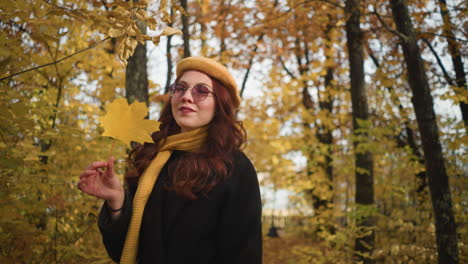 elegant lady in yellow beret twirling autumn leaf in hand while strolling through vibrant park surrounded by golden foliage, enjoying peaceful nature and crisp fall air with a graceful smile