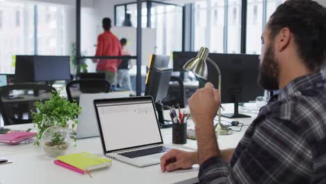 hombre caucásico sentado en el escritorio viendo el procesamiento de datos de codificación en la pantalla del portátil