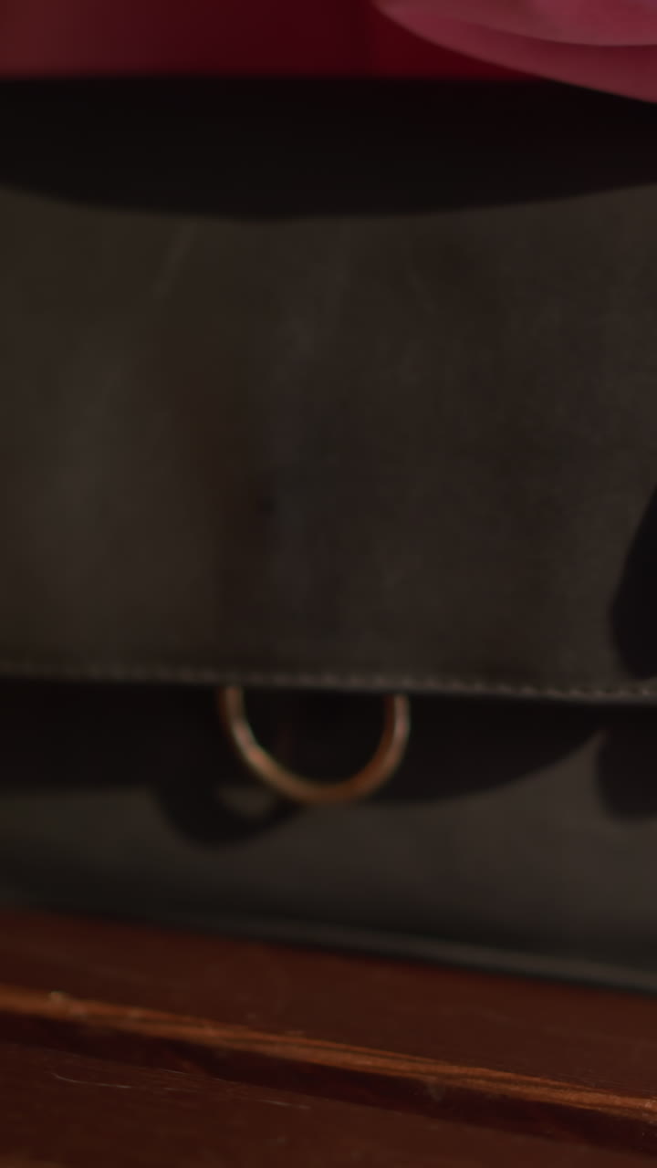 Blur view of red, green, and mint green shopping bags placed on a brown wooden bench by a lady in a pink dress, who sits down with a black handbag at her side, crosses her leg as she sits down