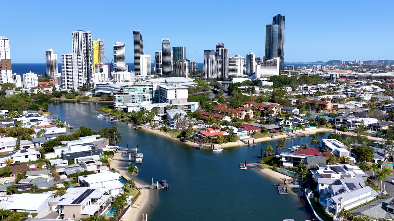 Drone glides above river, residential homes, and skyscrapers under bright daylight in Gold Coast
