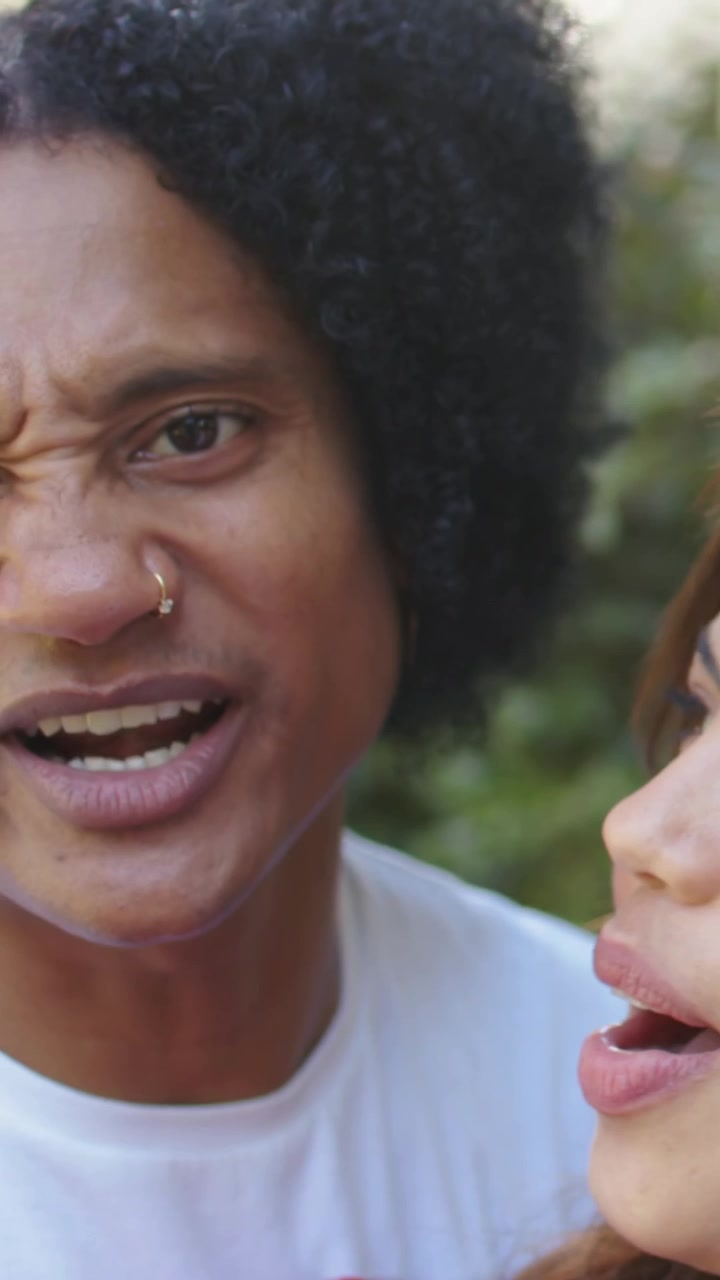 Vertikal video: Læbesynkroniserende duet, anden person kommer ind fra højre, kvinder i have, lyserød top og næsering.
